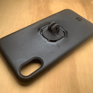 Puede incluir: Funda de teléfono negra con un soporte integrado para una cámara GoPro.