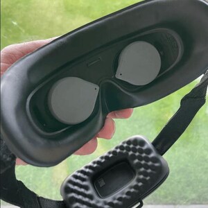 May include: Black VR headset with two gray lens covers and a black strap. The headset has a textured, padded section on the strap.