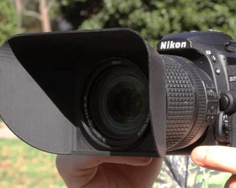 May include: A black Nikon D7500 camera with a lens attached. The camera has a lens hood attached to the lens.