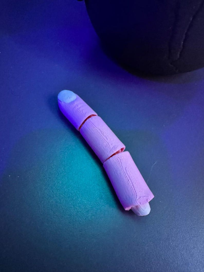 May include: A segmented, light purple finger model with a light blue fingernail. The finger is broken into three sections, with visible wood grain texture. The model is resting on a dark blue surface.