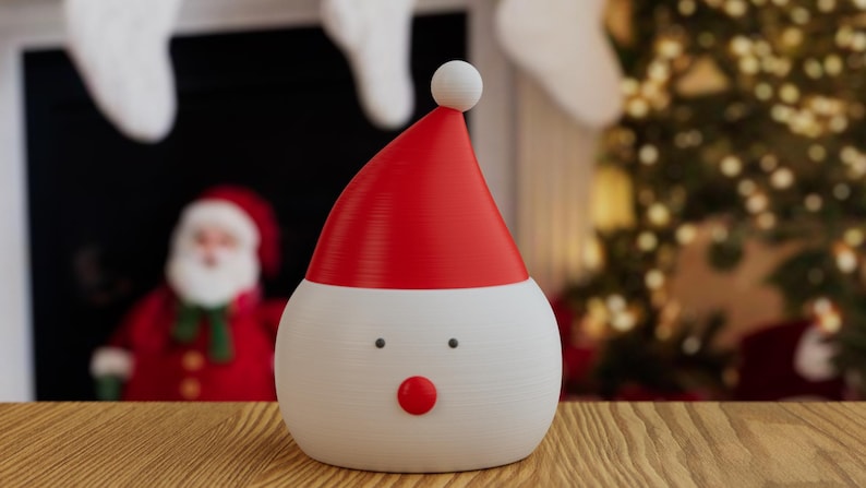 May include: A festive Christmas decoration shaped like Santa Claus. The figure has a white body, a red hat with a white ball on top, and a red nose. The background includes a blurred image of a Christmas tree and a Santa Claus figure.