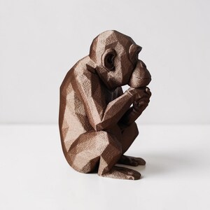 May include: A brown geometric chimpanzee sculpture in a seated position, holding its chin. The sculpture has a faceted design, giving it a modern, angular appearance. The chimpanzee is a decorative item, suitable for home decor.