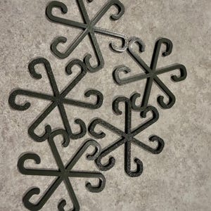 May include: A collection of six dark green, snowflake-shaped decorative items. Each piece features six curved arms extending from a central point, with a looped design at the end of each arm. The items are arranged on a light gray surface.