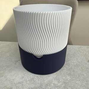 May include: A two-toned planter with a white, vertically ridged upper section and a deep navy blue base. The white section has a wavy pattern. The planter is designed for indoor or outdoor use.