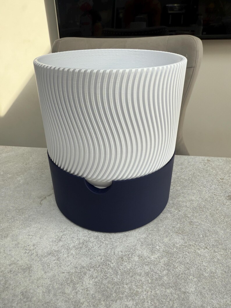 May include: A two-toned planter with a white, vertically ridged upper section and a deep navy blue base. The white section has a wavy pattern. The planter is designed for indoor or outdoor use.