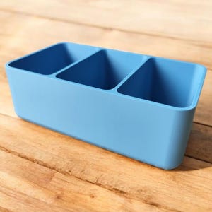 May include: A light blue plastic organizer with three compartments. The organizer is ideal for storing small items like pens, pencils, or other office supplies.