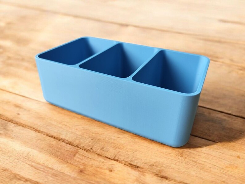 May include: A light blue plastic organizer with three compartments. The organizer is ideal for storing small items like pens, pencils, or other office supplies.