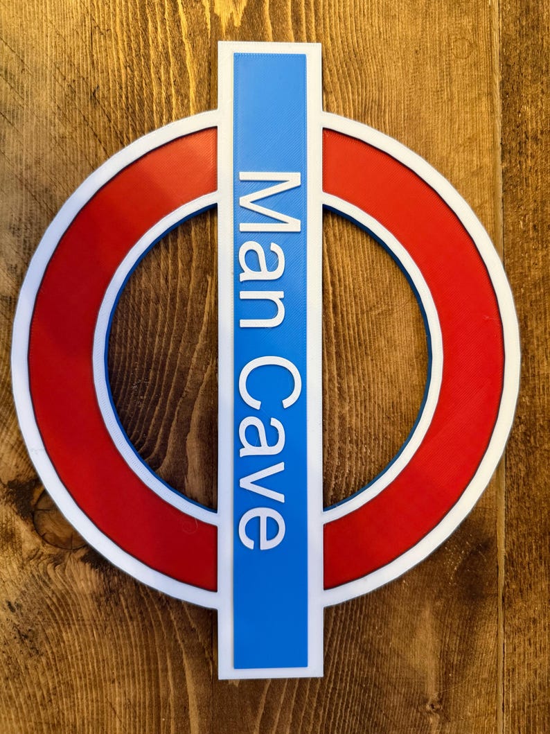 May include: A sign with a red circle, white border, and blue vertical rectangle. The words "Man Cave" are printed vertically in white on the blue rectangle. The sign is mounted on a wooden surface.