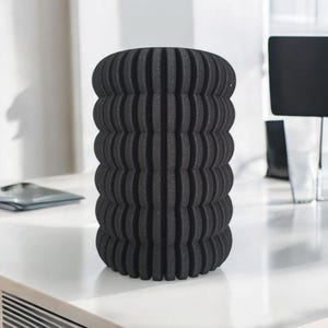 May include: A black cylindrical foam roller with a textured, ridged surface. The roller is designed for muscle recovery and self-massage. It is sitting on a white surface.