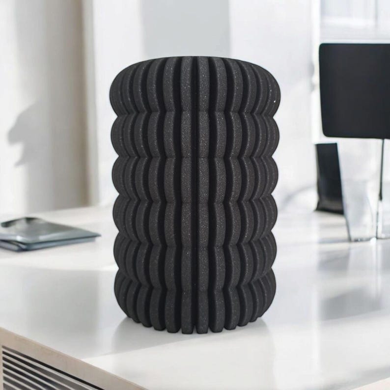 May include: A black cylindrical foam roller with a textured, ridged surface. The roller is designed for muscle recovery and self-massage. It is sitting on a white surface.