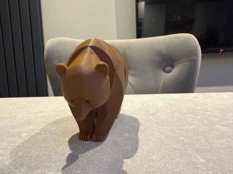 May include: A brown bear figurine with a geometric design. The bear is standing on all fours, with its head slightly lowered. The figurine is made of a solid material and has a smooth finish. The bear is a decorative item.
