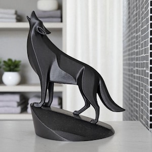 May include: A black wolf sculpture in a howling pose, mounted on a small, angled base. The figurine is set against a neutral background, showcasing the detailed form of the animal. The sculpture is likely made of a solid material.