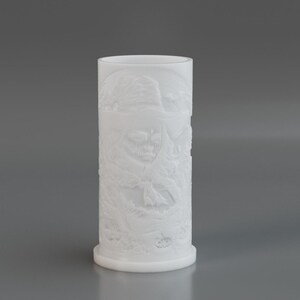 May include: A white cylindrical vase with a detailed relief pattern. The vase has a wide base and a smooth, rounded top. The relief design appears to depict a natural scene with various elements. The vase is made of a solid, opaque material.