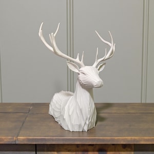 Puede incluir: Escultura de ciervo blanca con textura tallada detallada. El ciervo tiene grandes astas y est&aacute; en posici&oacute;n de descanso. La escultura es de material s&oacute;lido y est&aacute; sobre una superficie de madera. Ideal para decoraci&oacute;n del hogar.