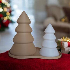 May include: Two ceramic Christmas tree decorations, one brown and one white, on a red surface. The trees are stylized and have a rounded, three-dimensional shape.