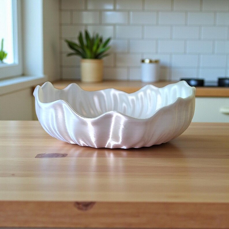 Puede incluir: Un cuenco de cer&aacute;mica blanco con borde festoneado. El cuenco tiene un acabado nacarado y est&aacute; sobre una superficie de madera. El entorno de la cocina incluye una ventana, una planta y un salpicadero de azulejos blancos.