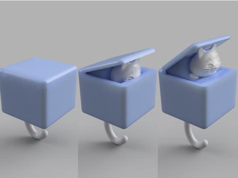 May include: A light blue cube-shaped hook with a white cat figurine inside. The cube has a hinged lid and a curved white hook. The cat figurine is white and has a smiling face.