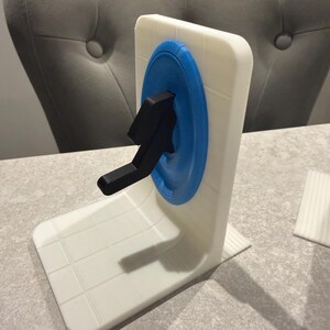 May include: A white and blue 3D-printed bookend featuring a black arrow design. The bookend has a square shape with a blue circle and a black arrow. The base is white with a grid pattern.