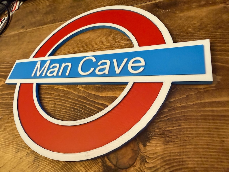 May include: A sign with a red circle and a blue rectangle, featuring the text "Man Cave" in white. The sign has a white border and is set against a wooden background.