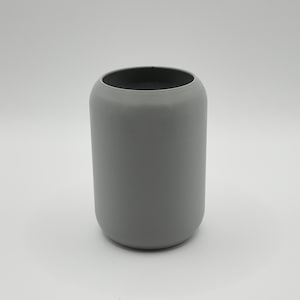 May include: A cylindrical, gray ceramic vase with a rounded top and a dark interior. The vase has a smooth, matte finish and a simple, modern design. The vase is suitable for holding flowers or as a decorative item.