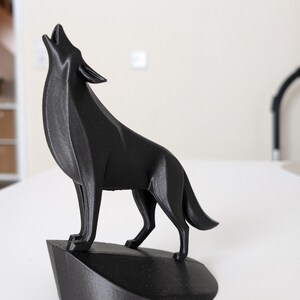 May include: A black, geometric-style wolf sculpture in a howling pose. The wolf is standing on a small, angled base. The sculpture is made of a solid, matte black material and is set against a neutral background.