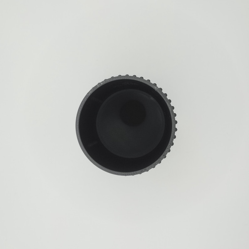 May include: A top-down view of a black cylindrical object with a textured, ridged exterior. The interior is a smooth, dark void. The object is set against a plain white background.