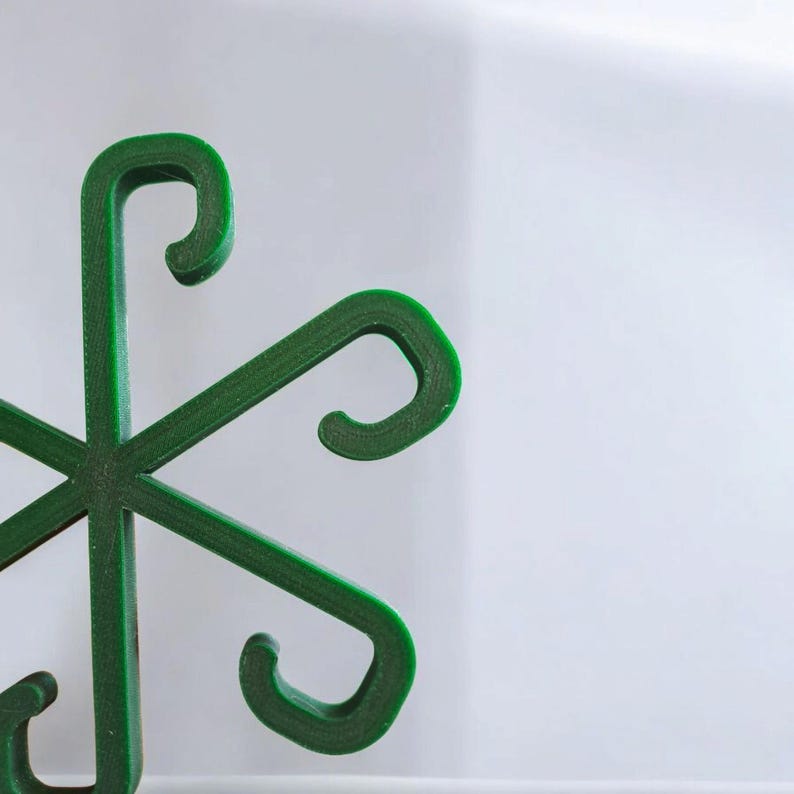 May include: A close-up of a green, six-pointed object with curved hooks at the end of each point. The object is made of a solid material and is set against a white background. The hooks are evenly spaced.