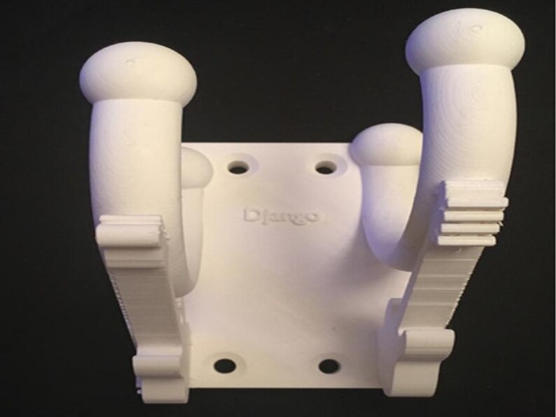 May include: White 3D-printed wall mount with two curved arms and a central mounting plate. The word "Django" is printed on the plate. The mount has a series of holes for screws.