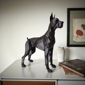 Puede incluir: Escultura geom&eacute;trica de perro negro con un dise&ntilde;o angular moderno. El perro est&aacute; sobre una superficie blanca. La escultura tiene una est&eacute;tica elegante y contempor&aacute;nea, adecuada para la decoraci&oacute;n del hogar. El fondo es neutro.