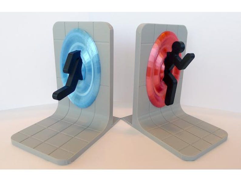 May include: A pair of gray bookends featuring a portal design. One bookend has a blue portal with a black figure, the other has a red portal with a black figure. The bookends have a curved base and a tiled pattern.