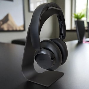 Peut inclure: Casque audio noir pos&eacute; sur un support noir assorti. Le casque est de conception moderne avec un bandeau et des oreillettes rembourr&eacute;s. Le support est minimaliste, avec un support incurv&eacute;.