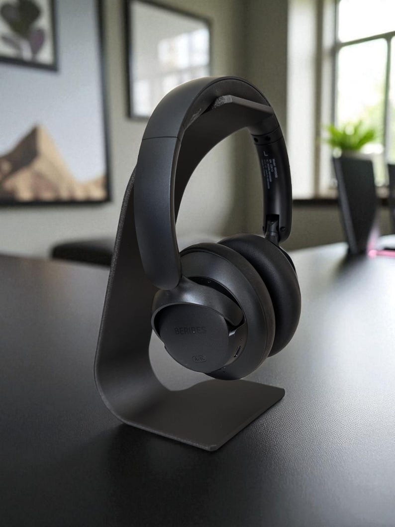 Peut inclure: Casque audio noir pos&eacute; sur un support noir assorti. Le casque est de conception moderne avec un bandeau et des oreillettes rembourr&eacute;s. Le support est minimaliste, avec un support incurv&eacute;.