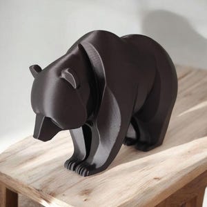 May include: A dark brown bear figurine with a geometric design. The bear is standing on all fours, with its head lowered. The figurine is placed on a light brown wooden surface.