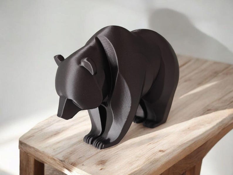 May include: A dark brown bear figurine with a geometric design. The bear is standing on all fours, with its head lowered. The figurine is placed on a light brown wooden surface.