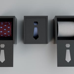 May include: Three dark gray boxes, each containing a rolled necktie. The first tie is red with a white and blue pattern. The second tie is blue with a subtle pattern. The third tie is white with a black pattern.