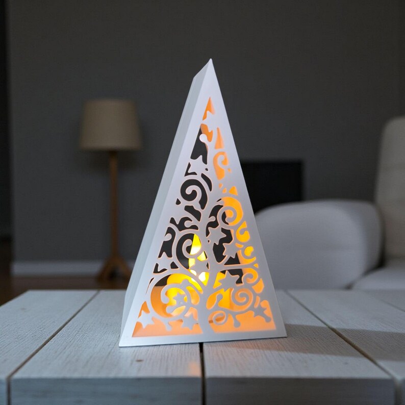 May include: A white, triangular lantern with intricate cut-out designs. The lantern is illuminated from within, casting a warm, orange glow. The design features swirling patterns and star-like shapes, creating a decorative lighting element.