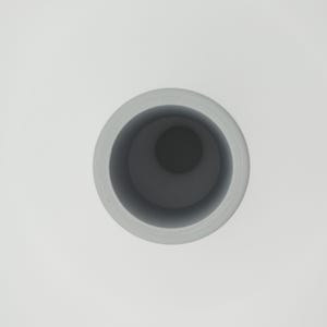May include: A light gray cylindrical vase with a dark gray interior, viewed from above. The vase has a smooth, matte finish and a simple, modern design. The interior is a deep, contrasting color.