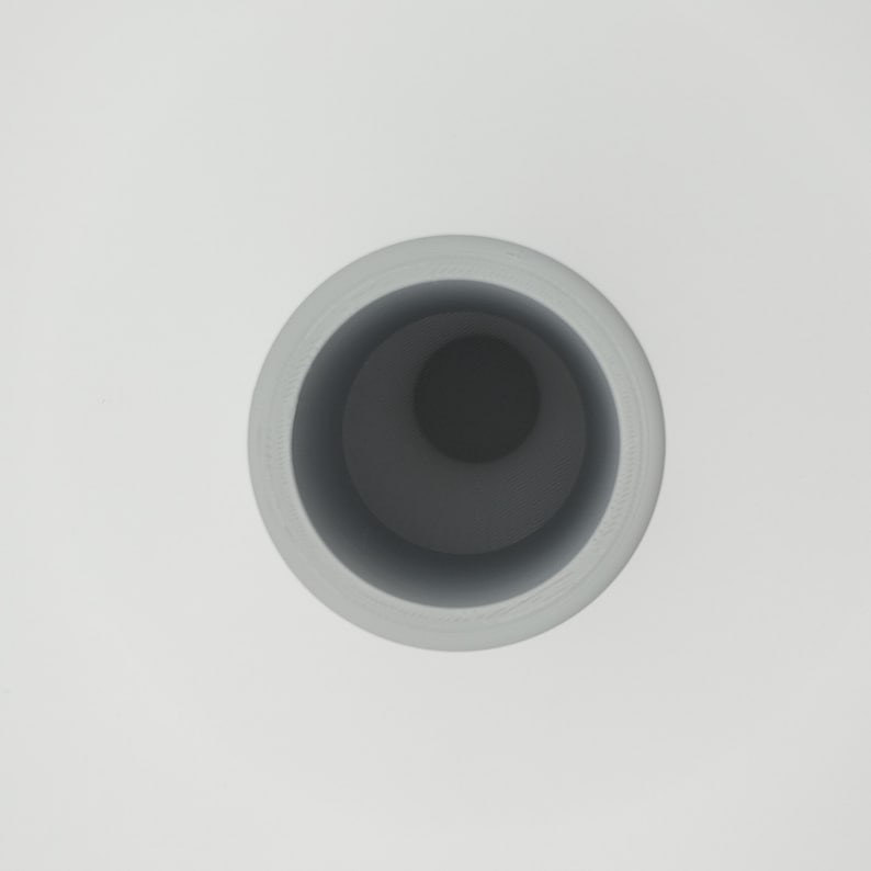 May include: A light gray cylindrical vase with a dark gray interior, viewed from above. The vase has a smooth, matte finish and a simple, modern design. The interior is a deep, contrasting color.