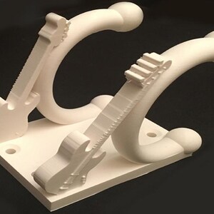 May include: Off-white guitar-shaped wall hooks. The hooks are mounted on a square base with pre-drilled holes for easy installation. The design features a stylized guitar shape, with the neck of the guitar curving into the hook.