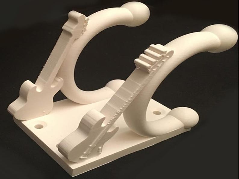 May include: Off-white guitar-shaped wall hooks. The hooks are mounted on a square base with pre-drilled holes for easy installation. The design features a stylized guitar shape, with the neck of the guitar curving into the hook.