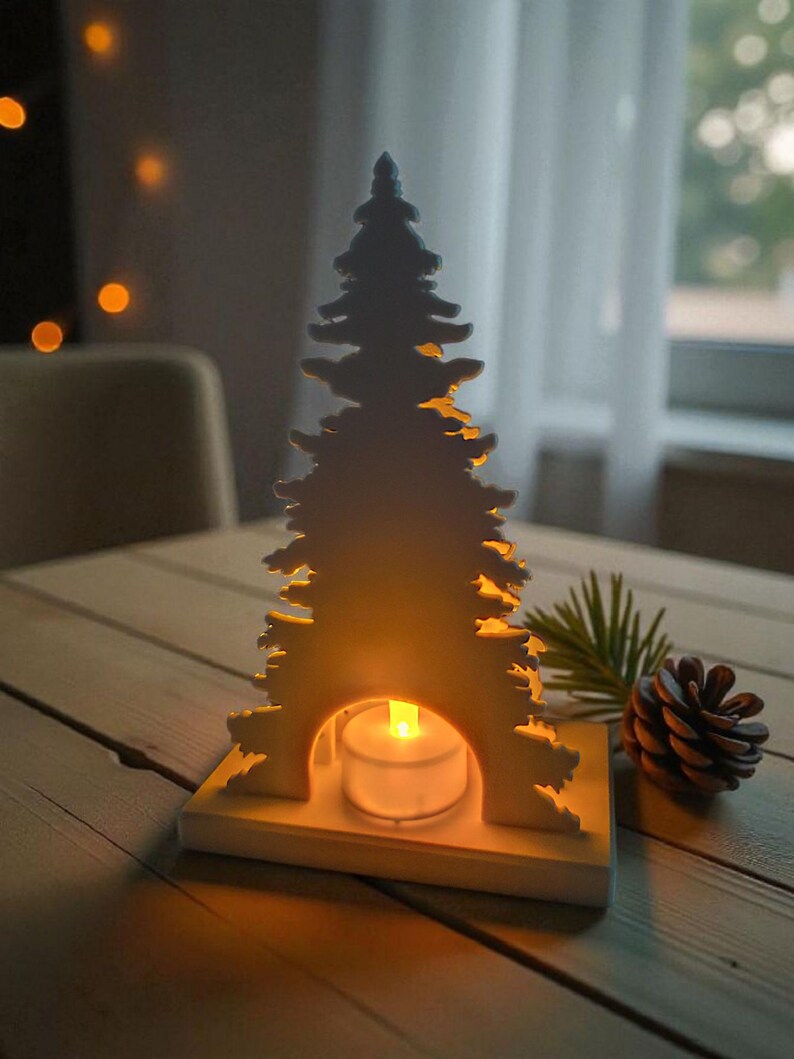 May include: A white wooden Christmas tree-shaped candle holder with a lit tea light inside. The candle holder is on a wooden table, next to a pine cone and a sprig of greenery. The background is blurred.