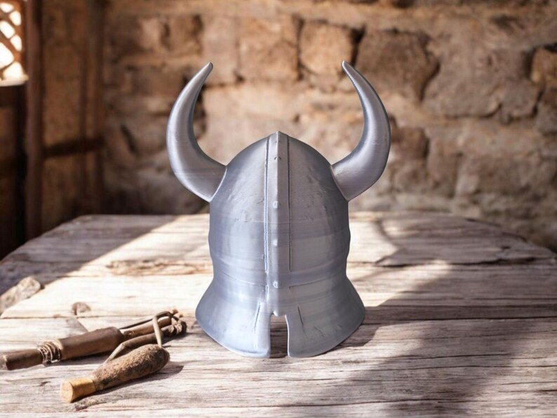 May include: A silver-colored Viking helmet with curved horns, resting on a wooden surface. The helmet is the focal point, showcasing its design and craftsmanship. The background features a rustic stone wall, enhancing the historical theme.