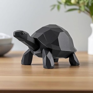 May include: A black geometric tortoise sculpture. The decorative figurine has a faceted design, giving it a modern look. The tortoise is made of a solid material and is displayed on a wooden surface. The sculpture is a decorative home accent.