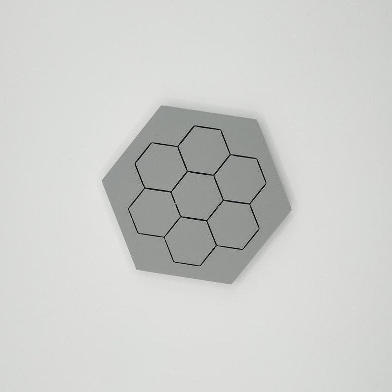 May include: A grey, hexagonal coaster with a honeycomb design. The coaster features a series of black outlines of hexagons arranged in a central pattern. The coaster is a solid grey colour.