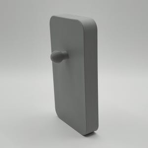 K&ouml;nnte beinhalten: Ein graues, rechteckiges Objekt mit abgerundeten Ecken und einem kleinen, strukturierten Knopf, der von einer Seite herausragt. Das Objekt ist ein solides, monochromes Design, wahrscheinlich ein T&uuml;rgriff oder eine &auml;hnliche Hardware.