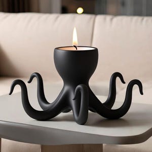May include: A black octopus-shaped candle holder with a lit candle. The candle holder has eight curved tentacles and a central cup to hold the candle. The design is modern and sculptural, suitable for home decor.