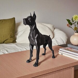 Puede incluir: Una escultura de perro geom&eacute;trico negro con un dise&ntilde;o moderno. El perro est&aacute; de pie sobre una superficie marr&oacute;n claro. La escultura tiene una apariencia facetada, con &aacute;ngulos agudos y l&iacute;neas limpias. Las orejas del perro est&aacute;n levantadas y tiene una mirada enfocada.