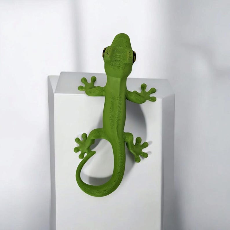 May include: A bright green lizard sculpture with a textured surface, clinging to a white, geometric block. The lizard has detailed features, including small black eyes and a curled tail. The sculpture is a decorative item.
