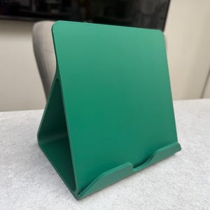 May include: A vibrant green tablet stand. The stand has a triangular base and a slightly angled back, with a small lip at the bottom to hold a tablet. The stand is made of a solid material and is designed to hold a tablet upright.