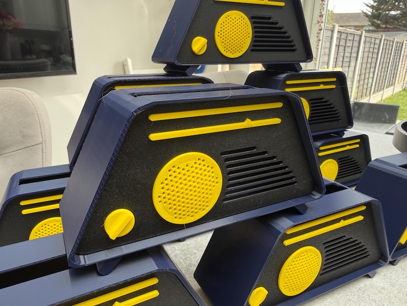 May include: A collection of navy blue and yellow geometric boxes. Each box features a yellow circular speaker and a yellow knob. The boxes are stacked, showcasing their design and color scheme. The overall aesthetic is modern and industrial.